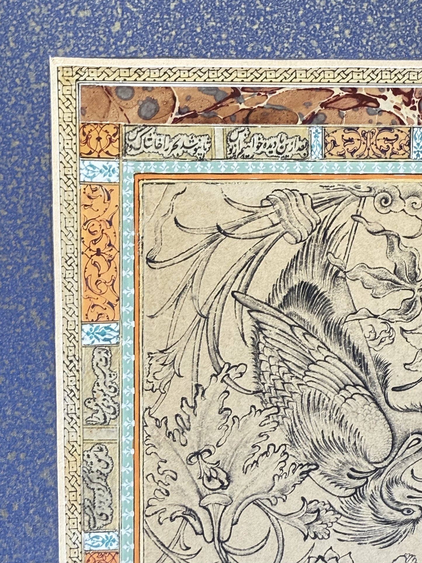 Detail of the siyah-qalam panel corner - a long-tailed crested bird drawn in fine black ink, its wing feathers closely scaled, moving through curling khataei foliage, framed by orange marbled paper, gold arabesque cartouches, turquoise micro-bands and a gold interlace rule. Muraqqa': The Gold Shamseh, Kamal al-Din Ghotb.