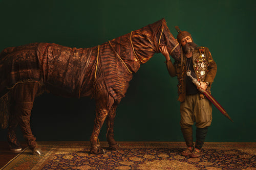 Reza Daryakenari's "Man in Ornate Armor" Stage Photography. Bearded man with sword and horse against a green wall.