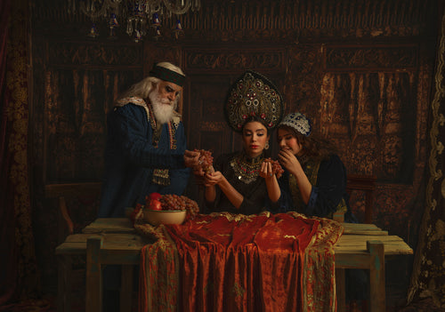 Man in blue robes offers grapes to women. Stage photography by Reza Daryakenari, printed on Epson canvas with varnish.