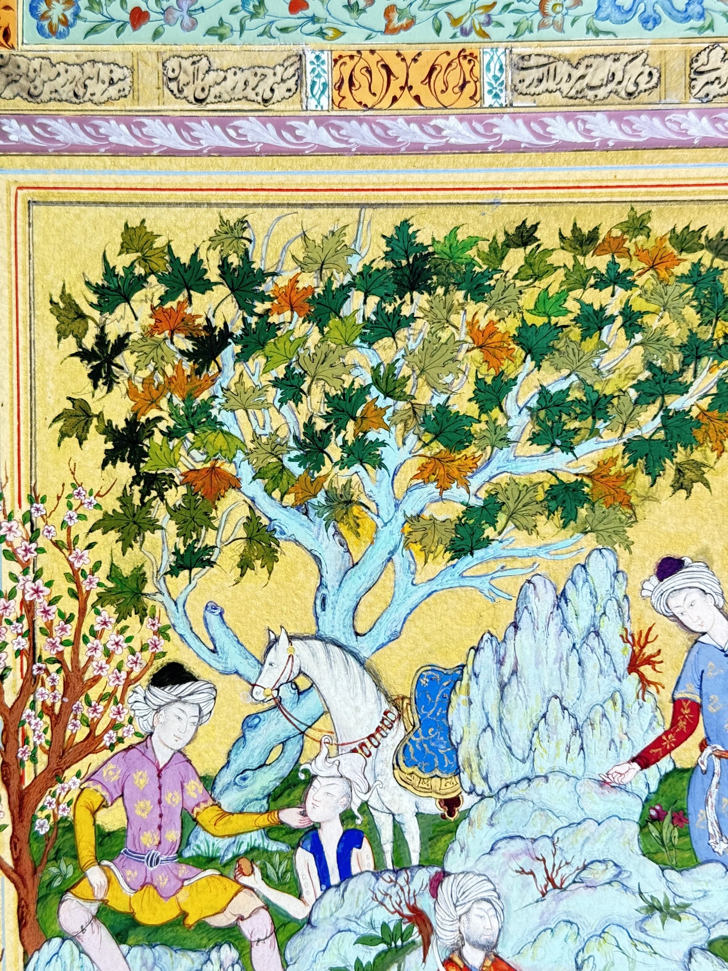 Detail of the falconry scene painted on a gold ground - turbaned figures in red, orange, blue and purple robes, a white horse in a blue saddlecloth with a gold-mounted saddle, a falcon held on a gloved wrist, a pale blue rock formation, a blossoming tree and a plane tree turning to autumn. Muraqqa': The Gold Shamseh, Kamal al-Din Ghotb.